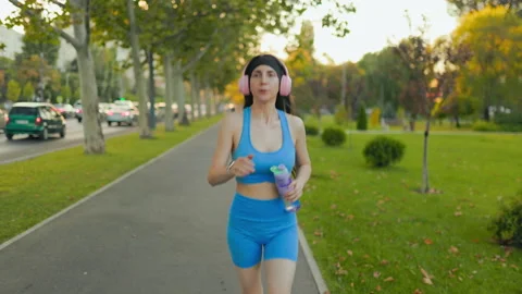 Active woman running on the park path with headphones and water bottle. Video stock 342597162