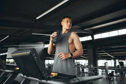 Active young guy in grey tshirt drinking water from bottle, standing on Stock Photos