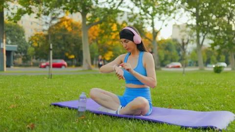 Active young woman checking her smartwatch on a yoga mat in the sunny park. Video stock 342599762