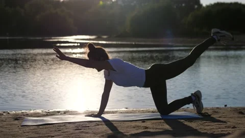 Active young woman doing exercise on sunset beach, the sun glare from the water Stock Footage 141782267