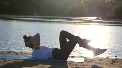 Active young woman doing exercise on sunset beach, the sun glare from the water Video stock 141782336