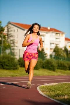 Active young woman runs on atheltic track on summer afternoon Stock Photos