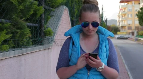 Active young woman writes a message using smart phone walking down the street  Stock Footage 62479379
