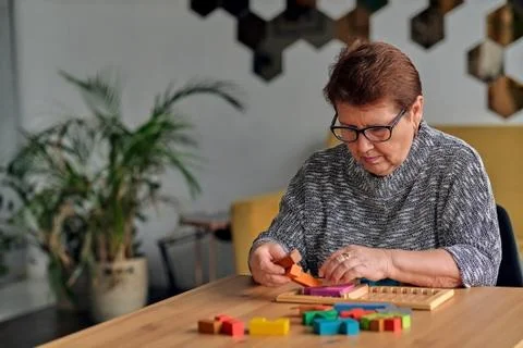 Activity can improve brain function. Elderly woman sitting at table and sorting Stock Photos