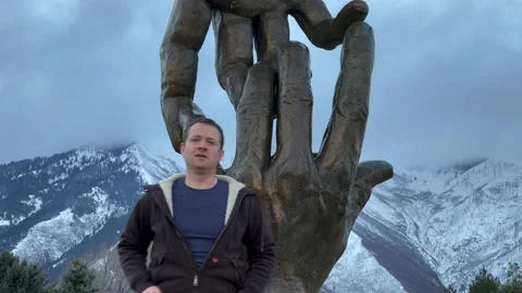 Actor or Tourist Stands in front of Large Hands Statue - Mountains in Background Vídeos de archivo 150883864