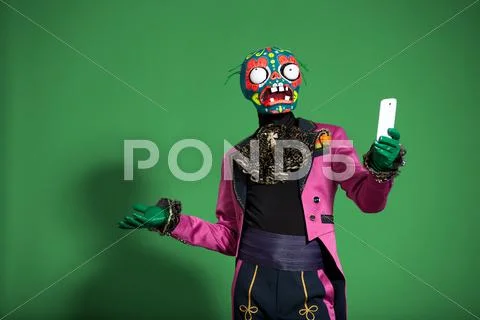 Actor In Pink Suit And Zombie Mask Poses On Green Background Taking Selfie
