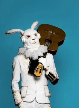 Actor posing in white rabbit suit playing guitar with earphones on blue Stock Photos