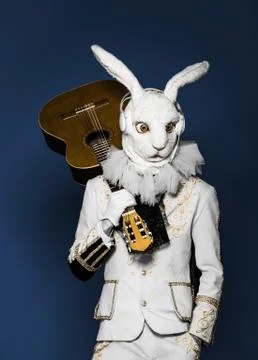Actor posing in white rabbit suit playing guitar with earphones on blue Stock Photos