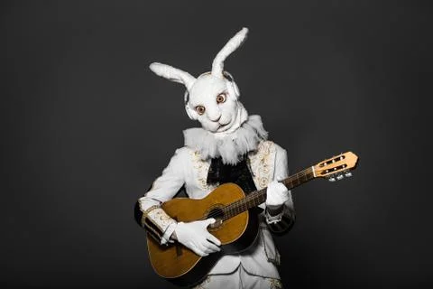 Actor posing in white rabbit suit playing guitar with earphones on black Stock Photos