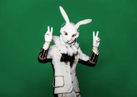 Actor posing in white rabbit suit with earphones on  green background.Studio Stock Photos