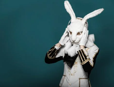 Actor posing in white rabbit suit with earphones on  blue background.Studio shot Stock Photos