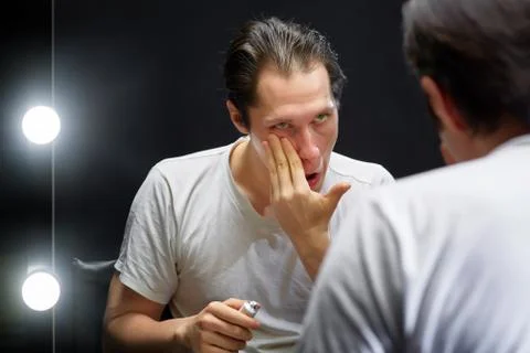 The actor sits in front of a mirror in a dark room Stock Photos