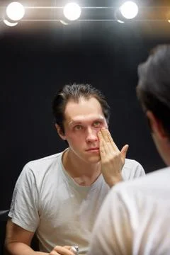 The actor sits in front of a mirror in a dark room Stock Photos