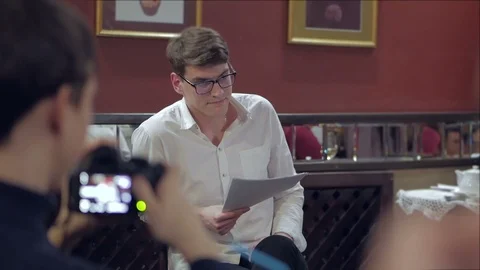 The actor, sitting in front of the audience in a cozy interior, reads prose from Stock Footage 103169040