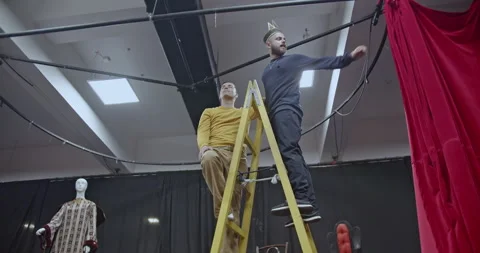 Actors Preparing the Stage: Hanging Red Curtains on a Black Metal Frame in a Stock Footage 312072930