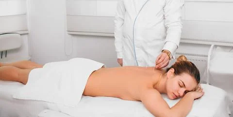 Acupuncturist inserting a needle into a female back. patient having traditi.. Stock Photos