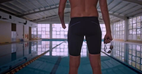 Adaptive amputee swimmer standing outside indoor pool holding goggles Stock Footage 146142924