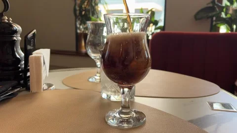 Add ice to cola pour cola over ice cubes in glass on walnut table with space for Stock Footage 284925870