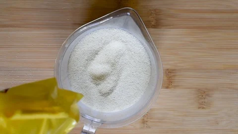 Add semolina in a measuring plastic Cup on the background of a wooden table Stock Footage 102754835