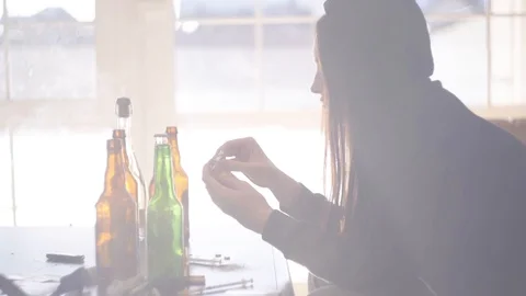 Addict sitting at a table with bottles of alcoholic beverages. Girl takes pills Video stock 111028578