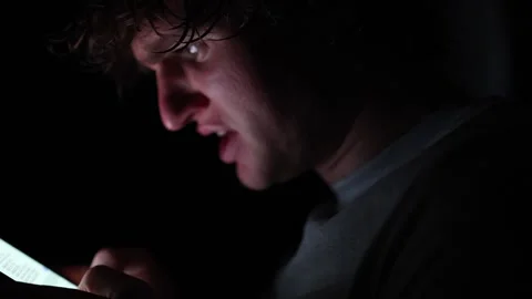 Addicted man stares into smartphone screen in total darkness lit only by the dev Stock Footage 313842917