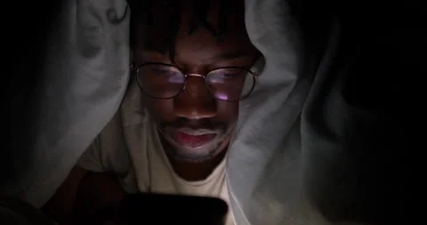 Addicted Young Man Under Bed Sheets Using Phone to Browse Social media Video stock 131368043