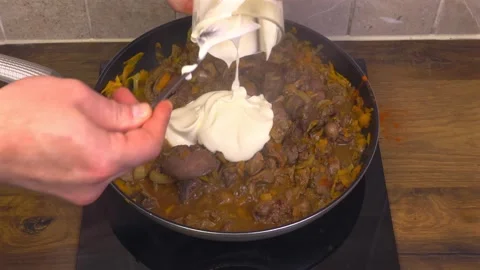 Adding and stirring sour cream with chicken gizzards and vegetables in pan Stock Footage 345422302