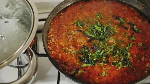 Adding basil and parsley in a pan with bolognese sauce Stock Photos