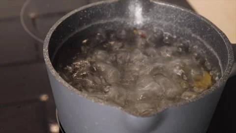 Adding bay leaf, cloves, and pepper to boiling water in a saucepan Stock Footage 303080169