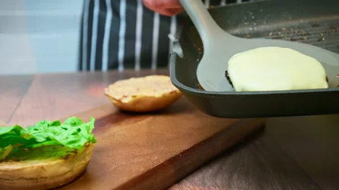 Adding a beef steak with cheese on top of a burger from a grilling pan in 4K. Stock Footage 153749749