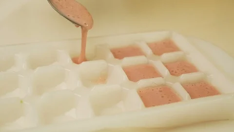Adding berry ice cream liquid to ice cube tray Stockbeeldmateriaal 124961244