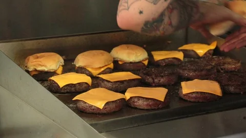 Adding buns on top of the burgers on a griddle Stock Footage 127716089