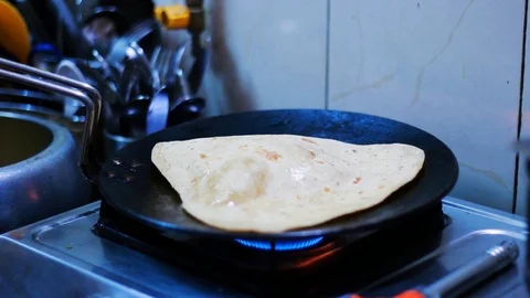 Adding butter and pressing preparing paratha over a gas stove flame. 스톡 동영상 123432140