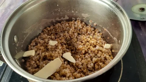 Adding butter to boiled buckwheat in a saucepan Stock Footage 231593994