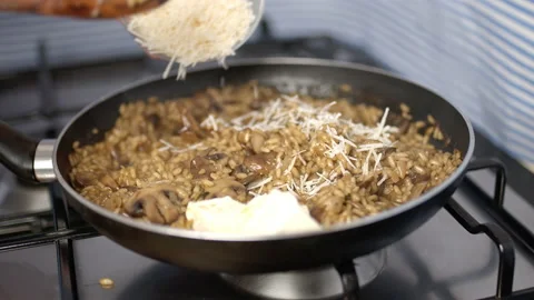 Adding butter cubes, grated parmesan cheese into the mushroom risotto in a pan. Stock Footage 134698853