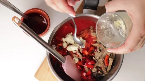 Adding butter into pot with cooked beef strips, tomato paste, fried bell peppers Stock Footage 317107363