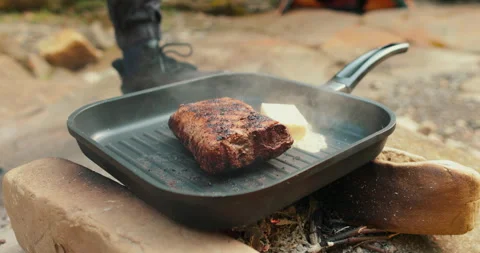 Adding butter to a steak on a hot pan in the process of grilling meat outdoors. Stock Footage 265151188