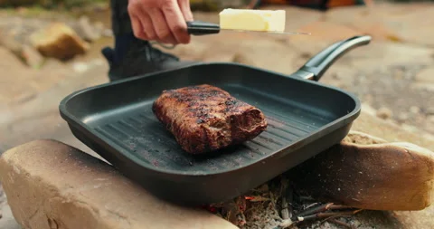 Adding butter to a steak on a hot pan in the process of grilling meat outdoors. Stock Footage 265151198