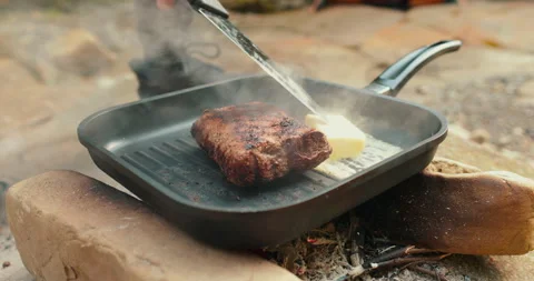 Adding butter to a steak on a hot pan in the process of grilling meat outdoors. Stock Footage 265151381