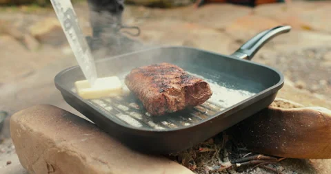 Adding butter to a steak on a hot pan in the process of grilling meat outdoors. Stock Footage 265151396
