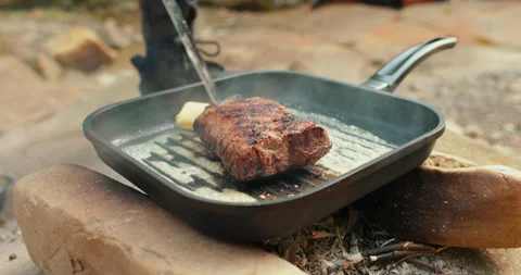 Adding butter to a steak on a hot pan in the process of grilling meat outdoors. Stock Footage 265151585