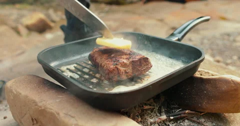 Adding butter to a steak on a hot pan in the process of grilling meat outdoors. Stock Footage 265151609