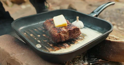 Adding butter to a steak on a hot pan in the process of grilling meat outdoors. Stock Footage 265151772