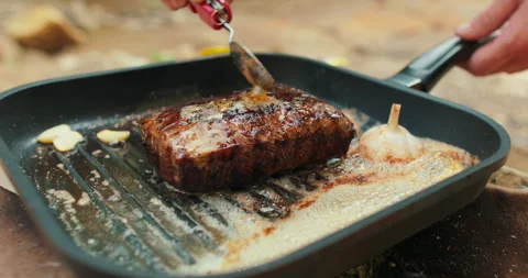 Adding butter to a steak on a hot pan in the process of grilling meat outdoors. Stock Footage 265152271