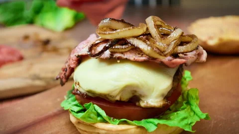 Adding caramelised onion rings on a beef steak with cheese on top of a burger. Stock Footage 153749863