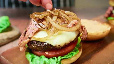 Adding caramelised onion rings on a beef steak with cheese on top of a burger. Stock Footage 153762350