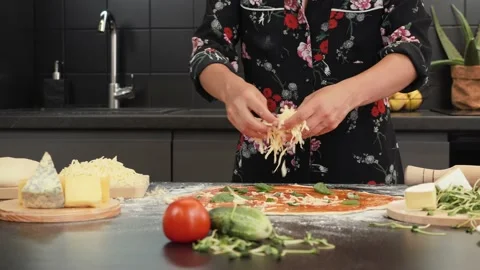 Adding cheese to pizza on wooden table. Hands scattering cheese over pizza Stock Footage 157544002