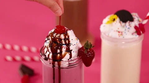 Adding Cherry to Strawberry Milkshake with Whipped Cream and Chocolate Syrup Stock Footage 323058980