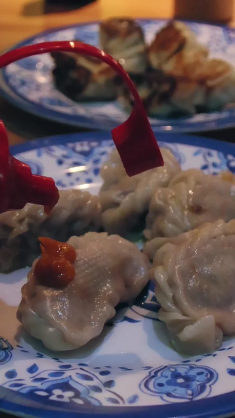 Adding chilli paste to a plate of steamed momo or Nepali dumpling Stock Footage 332596925