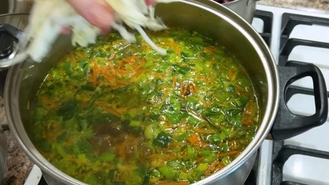 Adding chopped cabbage to a pot with potatoes, carrots and leek stems. 库存影片 302754588